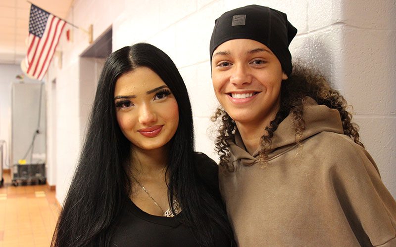 Two high school students smile. There is an American flag in the background.