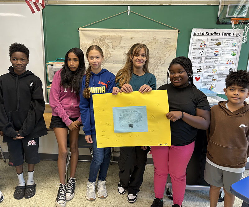 A group of six middle school students hold a yellow poster. On it is a pledge for no place for hate and their signatures.