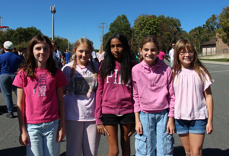 Five middle school girls wear pink and stand together outside.