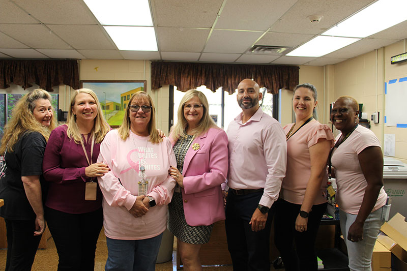 A group of seven adults, all dressed in pink. stand together and smile.