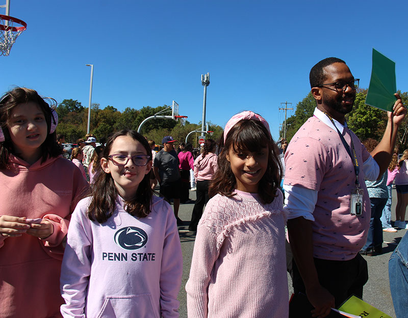 A man on the right wears a pink shirt, and there are three girls behind him also waring pink.