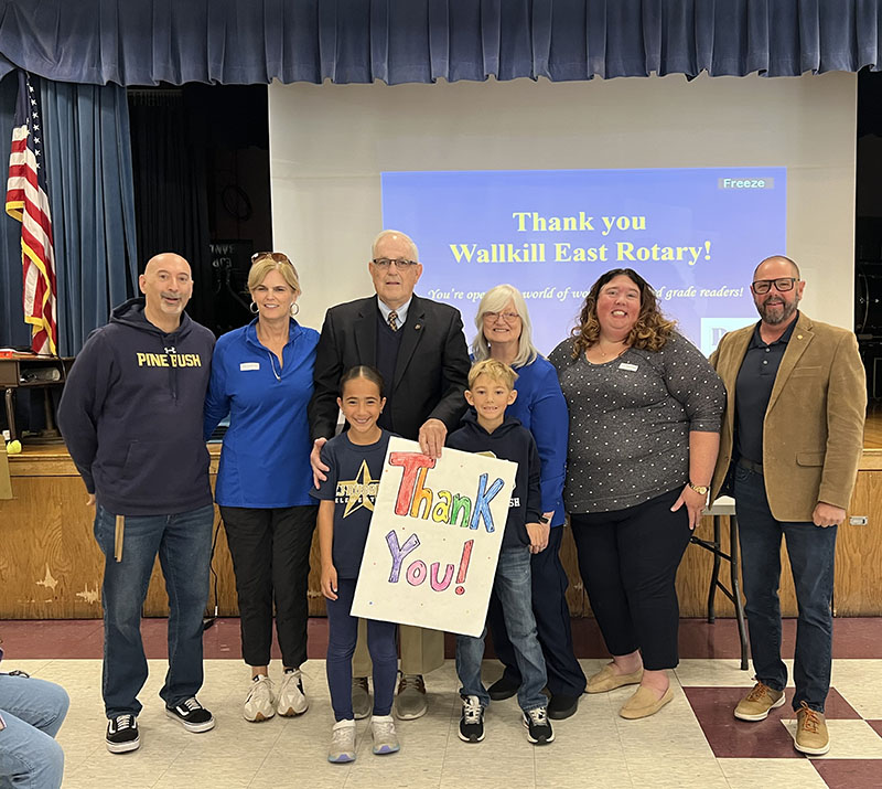Two third-grade students stand in front holding an oversized thank you card. Behind them are six adults. All are smiling.