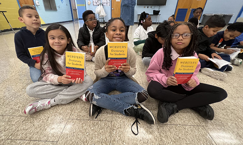Three third grade girls sit and hold up their new dictionaries.