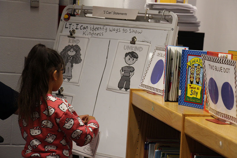 A first grade girl is up at a white board deciding where she should put her picture.