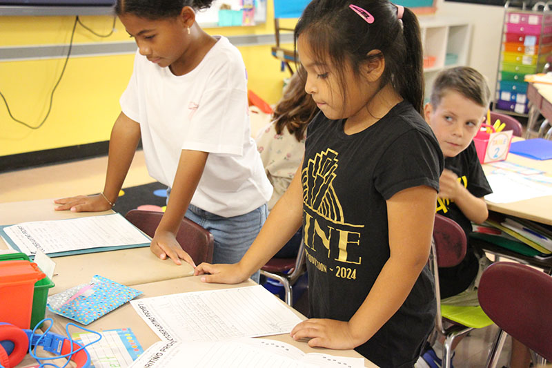 A third-grade girl wearing a black shirt reads from her essay.