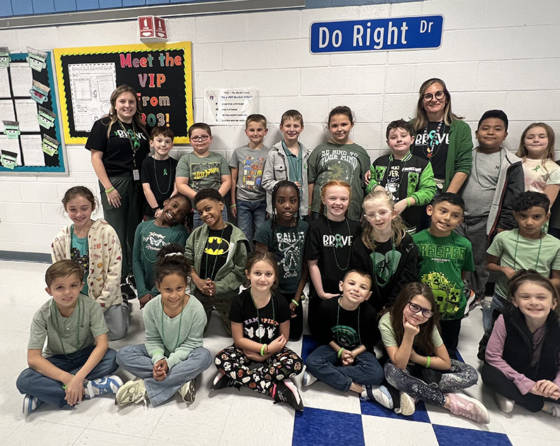 A group of about 20 third graders and two teachers. Most of the kids have green on.