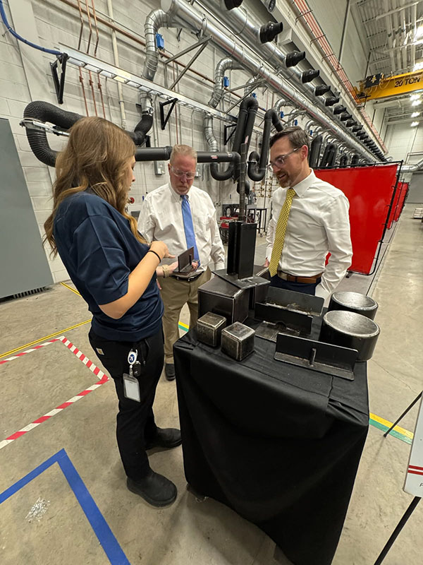 A woman shows a piece of equipment to two men, who listen.