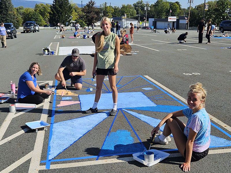 A group of high school students painting a parking spot several different shades of blue.