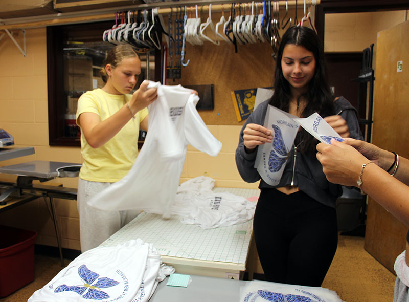 Two high school girls fold shirts and iron ons for tshirts.