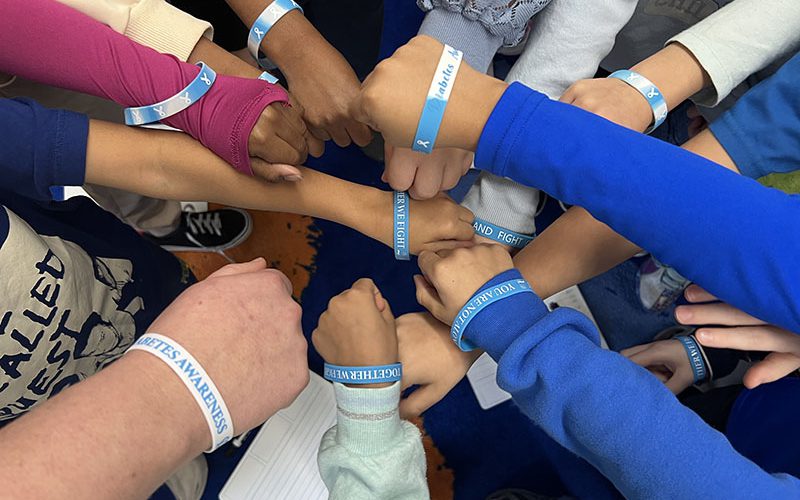 A large number of kids arms in a circle, all with blue bracelets for diabetes awareness.