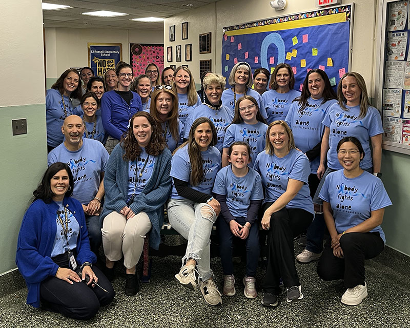 A large group of adults and some kids all wearing blue shirts for diabetes awareness smile.