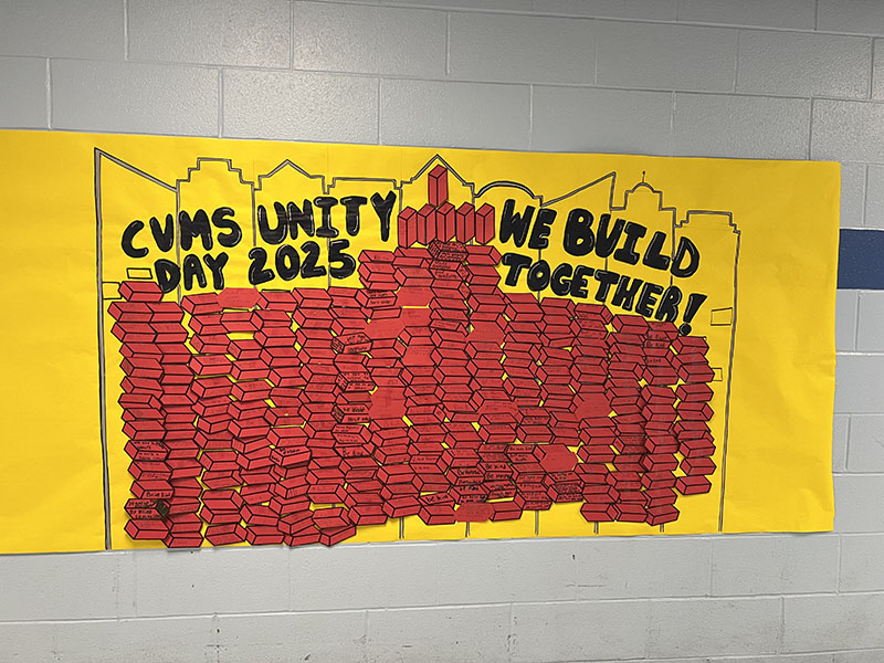 A large wall mural, yellow background filled in with red paper bricks. It says CVMS Unity Day 2025 We build togehter!