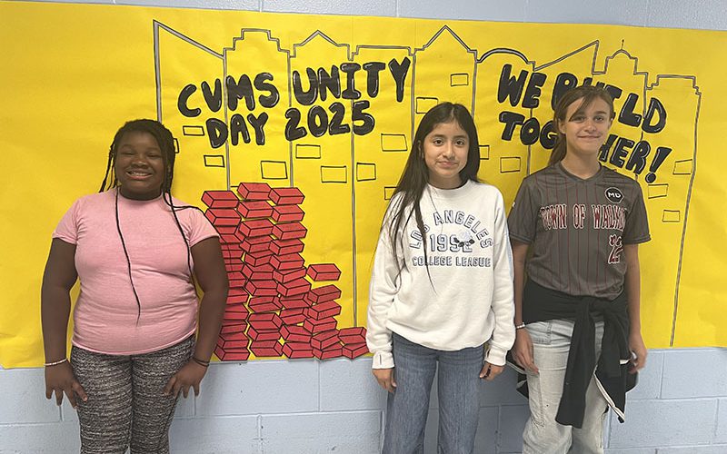 Three middle school kids stand next to the mural that has several red paper bricks on it. It is filling up.