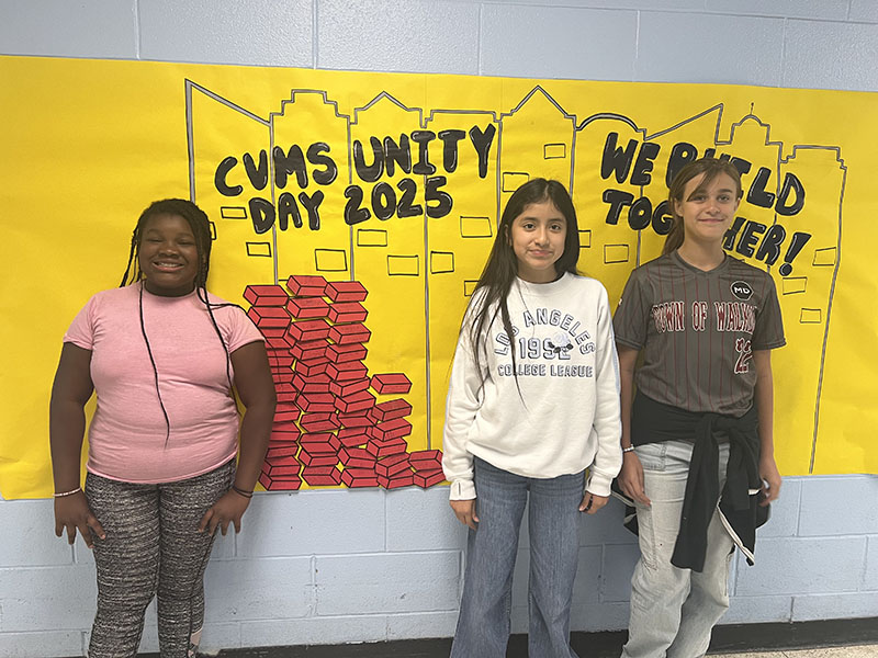 Three middle school kids stand next to the mural that has several red paper bricks on it. It is filling up.
