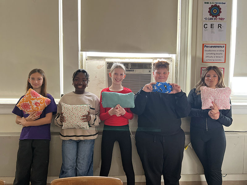 A group of five middle school kids hold up pillows they sewed in class. 
