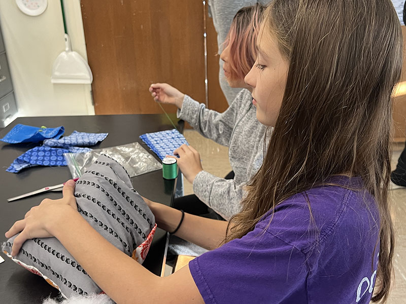 A middle school girl sews a pillow.