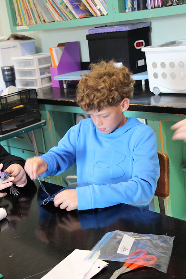 A boy wearing a bright blue shirt practices sewing stitches.