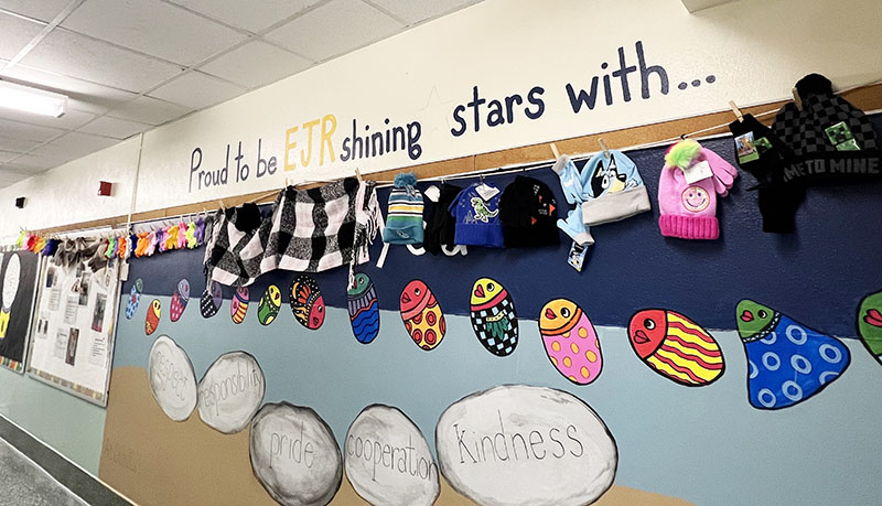 A line of colorful mittens, gloves, hats and scarves hang along a wall.