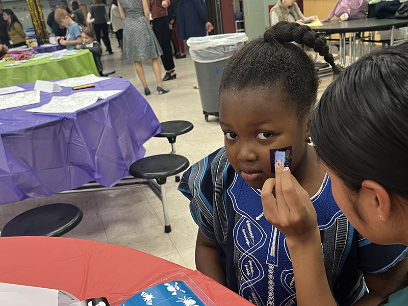 A young girl sits and gets her face painted.