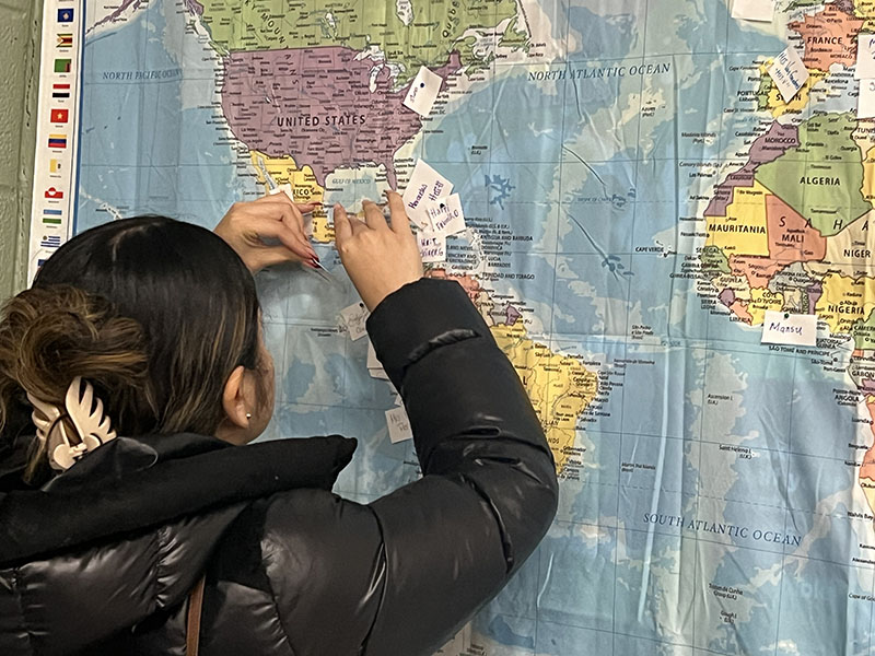 A young woman puts a flag on a large wall map.