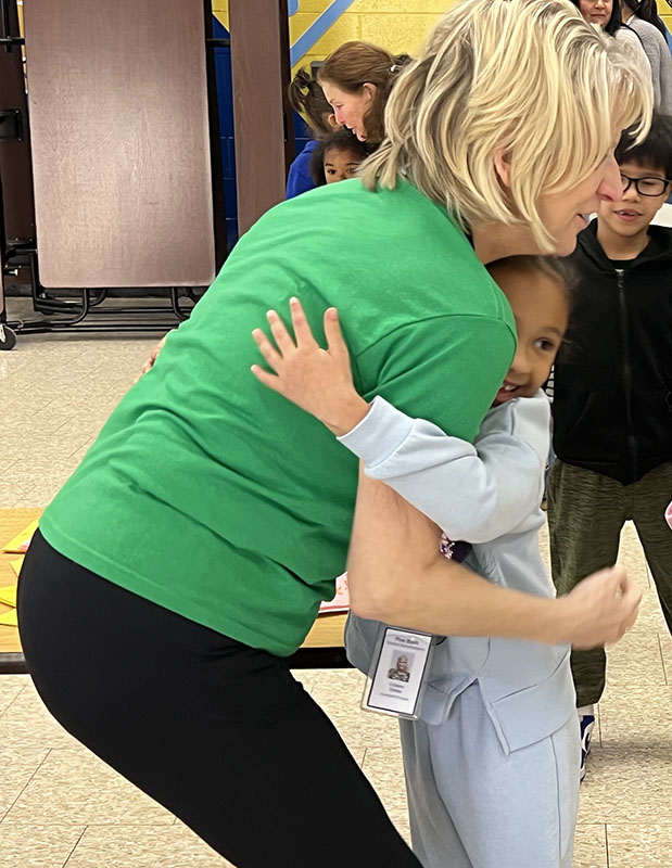 A woman with blonde hair wearing a green tshirt hugs a little girl dressed in blue.