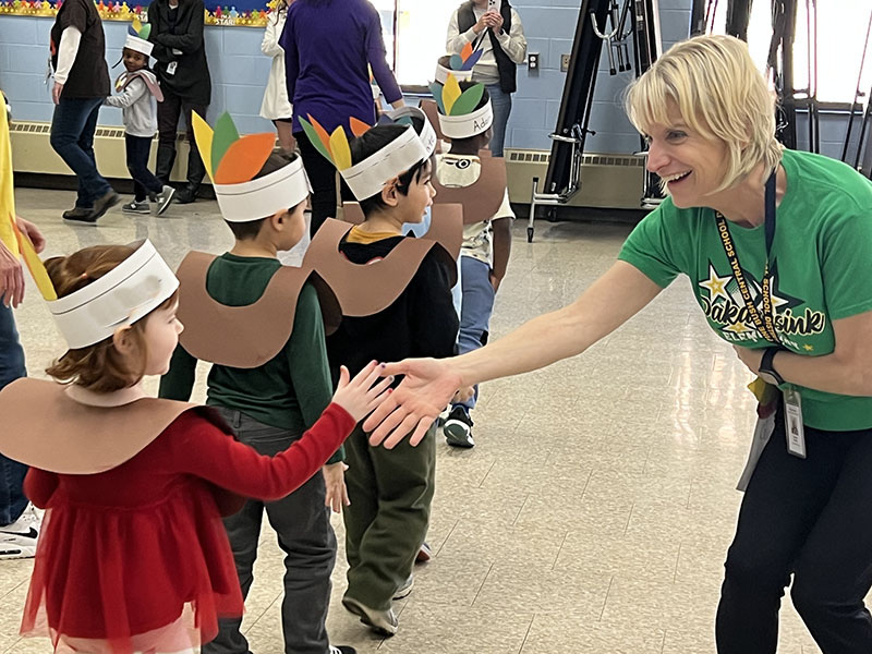 A woman in a green shirt puts her hand out to give high five to a little girl walking by.