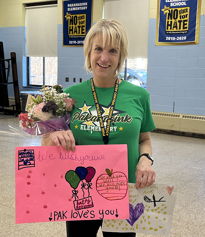 A woman with blonde hair smiles as she holds flowers and handmade cards from kids.