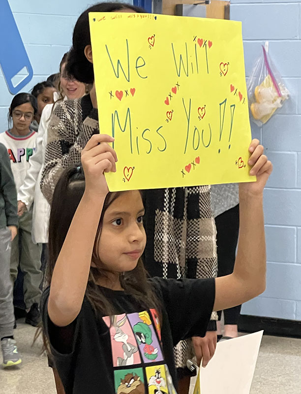 A little girl holds up a yellow sign that says We will Midd You!