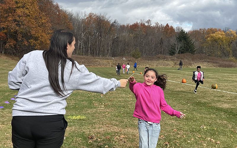 A girl wearing a pink sweatshirt takes a popsicle stick from a woman with long dark hair, wearing a gray sweatshirt.