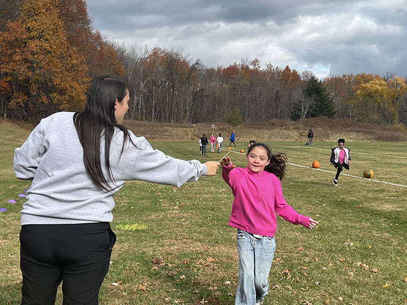 A girl wearing a pink sweatshirt takes a popsicle stick from a woman with long dark hair, wearing a gray sweatshirt.