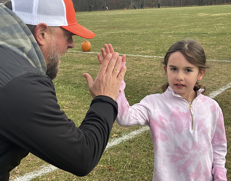 A girl in a pink and white sweatshirt gives high five to a man in a baseball cap.