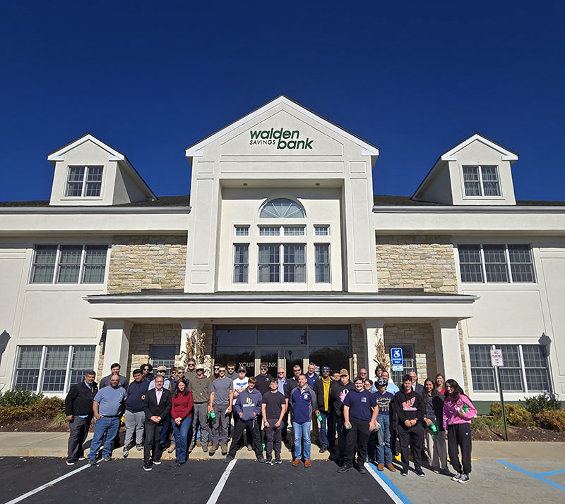 A large group of high school students stand outside of a bank.