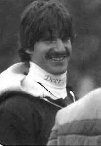 A black and white photo of a young man form the 1970s. He is smiling.