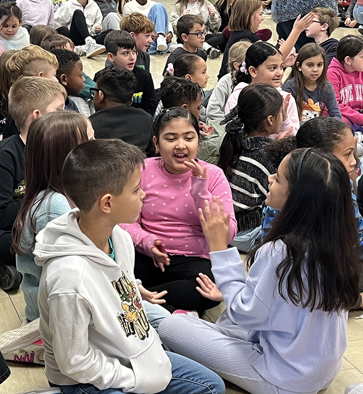 A group of kids sit on a floor having fun together.