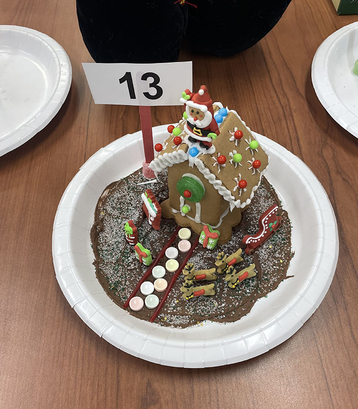A gingerbread house made with a chocolate ground, candy walkway and a Santa sitting on the roof.