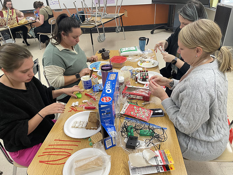 Women sit at a table making gingerbread houses.
