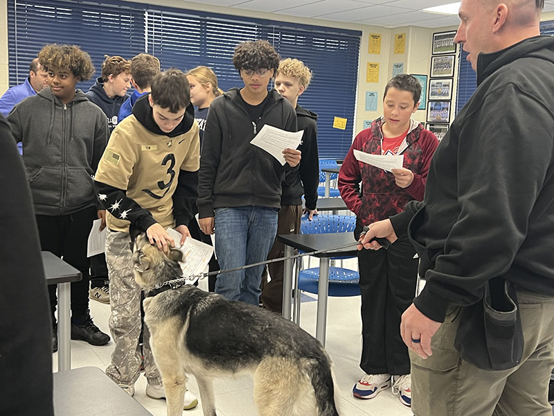 A group of middle school students pet a large German Shepard dog.