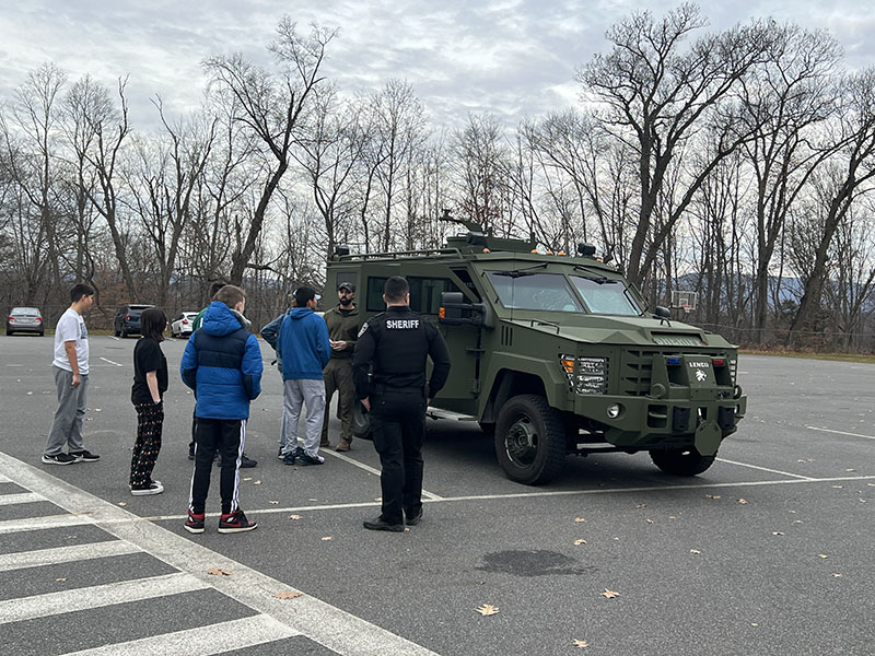 A large police vehicle in a parking lot with a cop outside explaining it to a group of students.