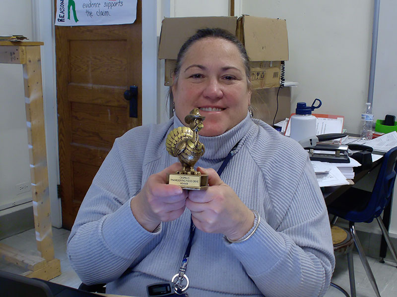 A woman smiles as she holds up a small trophy with a turkey on it.