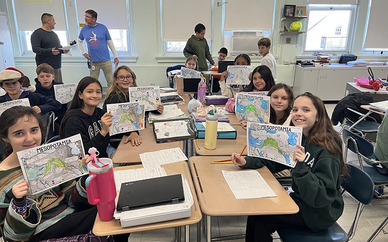 A group of eight middle school students hold up maps they colored of Mesopotamia.