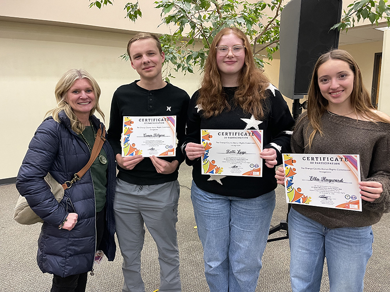 Three high schools students hold certificates and smile. With them is a woman.