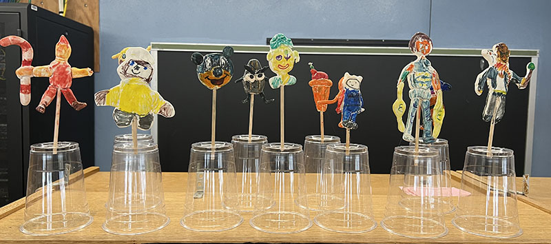 Small clay figures sitting on a stick, that is on a clear plastic cup.