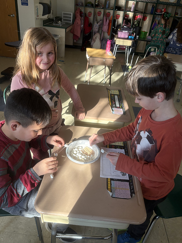 A group of younger elementary students build a bridge with toothpicks and marshmallows.
