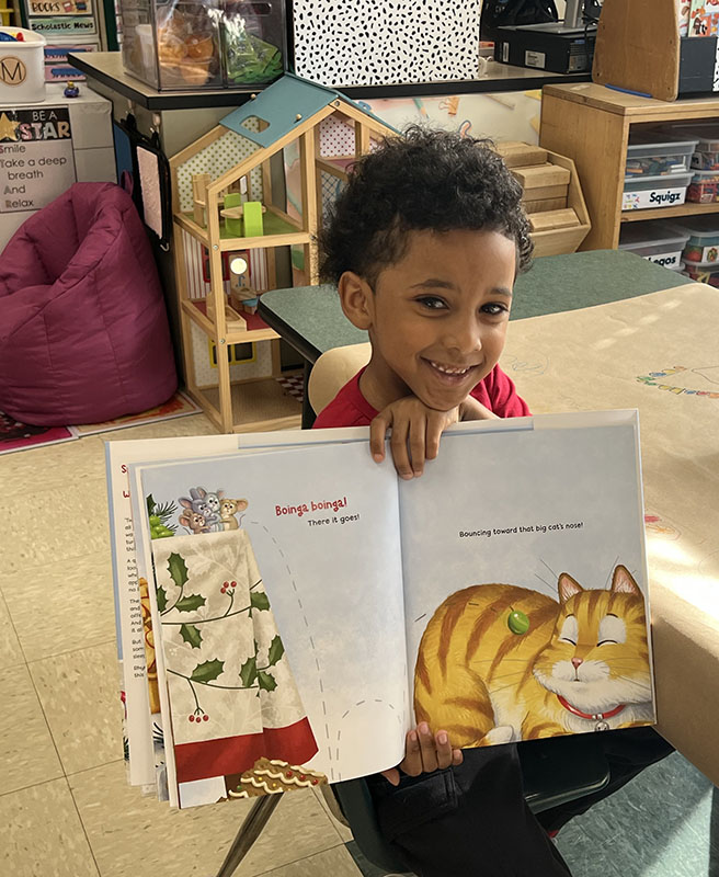 A little boy smiles as he holds a children's book open.