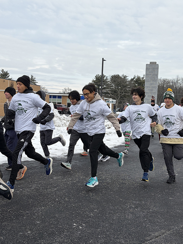 A group of high school kids, all wearing white tshirts that say tinsel trot, run on a track.
