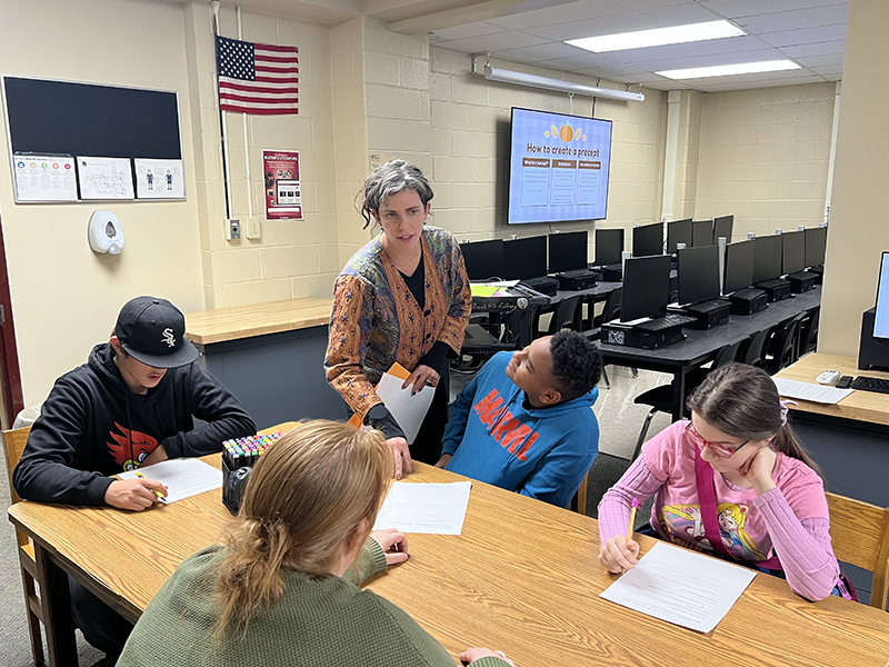A woman talks to several students working at a table.