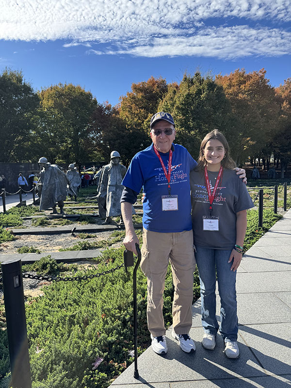 A young woman and an older man with a cane stand in front of a war memorial in Washington DC