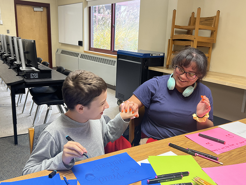 A woman gives a fistbump to a student who is drawing a picture.