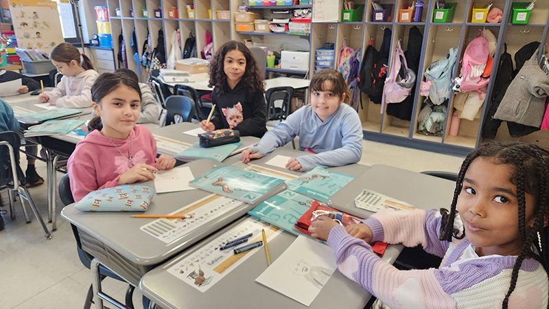 A group of second grade students sit at desks working on a project.