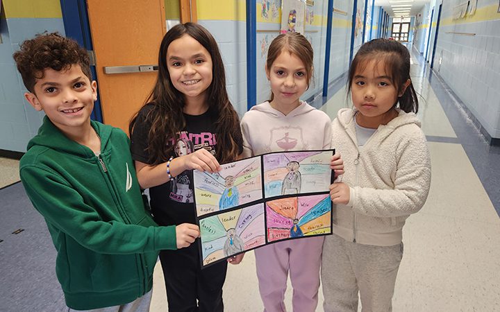 Four second grade students hold drawings of Martin Luther King Jr. and the words that describe him.